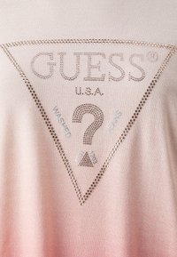 Chemise dégradé rose avec un design triangulaire comportant "GUESS U.S.A." en strass et du texte imprimé incluant "WASHED" et "JEANS."