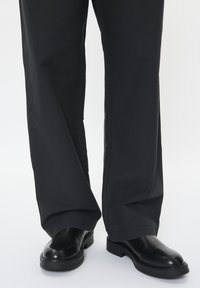 Pantalones de pierna ancha negros combinados con botas de tobillo de cuero negro. Los pantalones presentan una textura suave; las botas tienen una punta redondeada y suela gruesa.
