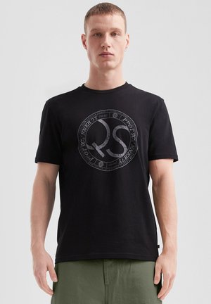 T-shirt en coton noir avec un col rond et des manches courtes. Présente un grand logo circulaire gris au centre.