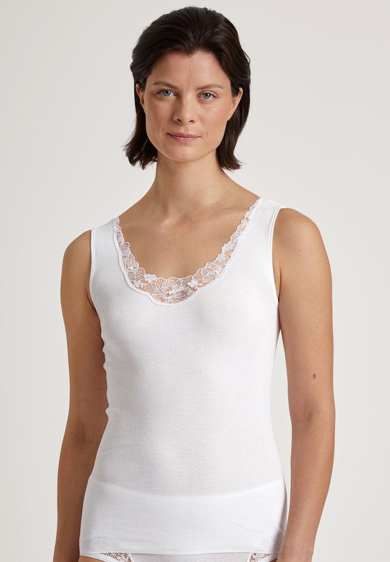 Top bianco senza maniche con dettagli in pizzo lungo il collo a V. Tessuto morbido e aderente con una texture liscia.