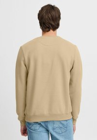 Beige crewneck sweatshirt lavet af blødt materiale med ribbede manchetter og kant. Simpelt, rent design uden synlige mønstre eller logoer.