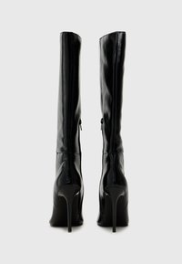 Bottes noires montantes en cuir brillant avec un design élégant, bout pointu et talon aigu de haute hauteur. Présentent une fermeture éclair sur le côté.