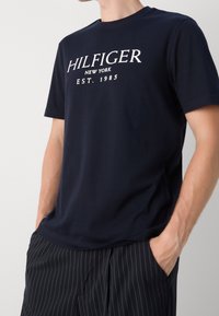 Navy T-shirt made of cotton featuring a white "HILFIGER NEW YORK EST. 1985" print across the chest. Short sleeves and a classic crew neckline.