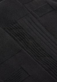 Primo piano di un tessuto nero con diversi modelli di lavoro a maglia che creano un design testurizzato a patchwork.