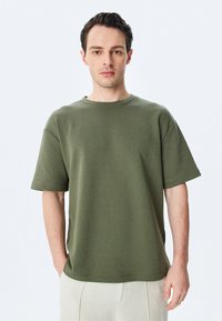 Olivenfarvet oversized T-shirt lavet af blødt stof, med rund hals og korte ærmer, i et ensfarvet design med minimale syninger.