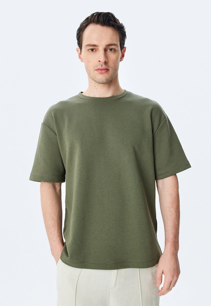 Olivenfarvet oversized T-shirt lavet af blødt stof, med rund hals og korte ærmer, i et ensfarvet design med minimale syninger.