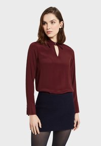 Burgundowa bluzka z długim rękawem, z kołnierzykiem na guziki i dekoltem w kształcie łezki, w połączeniu z fakturowaną granatową mini spódnicą.