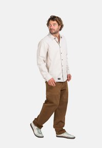 Light beige button-up shirt, brown cargo pants, and gray sneakers with white stripes. Features simple design and relaxed fit.