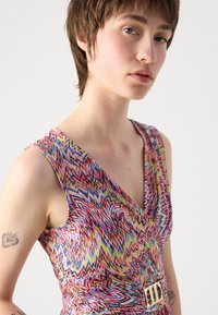 Robe multicolore présentant un motif en chevron, un décolleté en V et une taille froncée avec un détail de boucle en or. Tissu doux au toucher lisse.