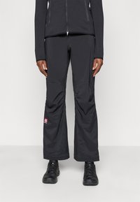 Pantalones de exterior negros con un ajuste relajado, que presentan un logo rojo en la parte inferior de la pierna, fabricados con un tejido ligero y de textura suave.
