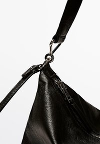 Borsa a tracolla in pelle nera con finitura opaca e chiusura con zip. Presenta un corpo testurizzato e connettori in metallo argentato. Tracolla regolabile inclusa.