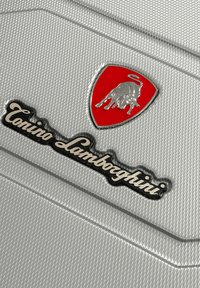 Superficie texturada plateada con un logo rojo y plateado de Lamborghini y el texto "Torino Lamborghini" en script negro debajo.