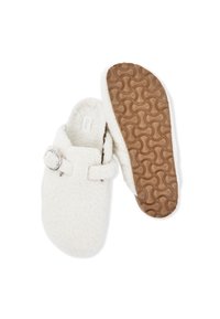 Pantofole bianche foderate in pile con punta rotonda, cinturino regolabile con fibbia e suola in gomma marrone stampata. La morbidezza del tessuto aumenta il comfort.