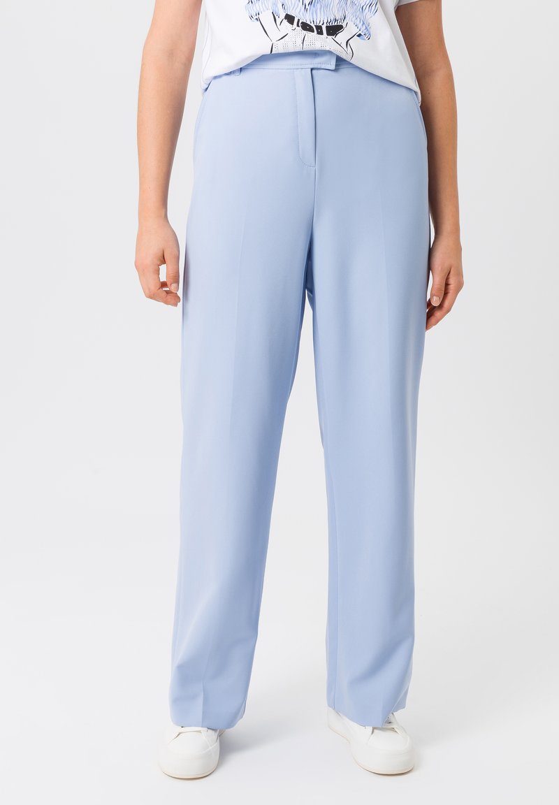 Lichtblauwe, wijde broek van soepele stof, met een op maat gemaakte snit en voorplooien, gecombineerd met witte sneakers.