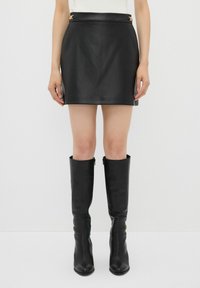 Zwarte leren mini rok met een gladde textuur en een gouden hardwareaccent op de tailleband, gecombineerd met zwarte leren laarzen tot aan de knie.