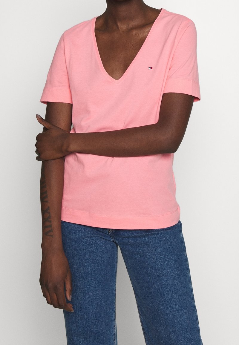 T-shirt rose à col en V en coton doux, à manches courtes, avec un petit logo sur la poitrine gauche. Assorti à un jean en denim bleu.