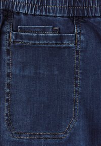 Dunkelblauer Jeansstoff mit einer hinteren Tasche, die eine geschwungene Oberkante und kontrastierende gelbe Nähte aufweist. Glatte Textur mit leichter Ausbleichung.