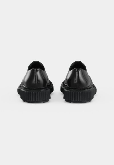 Paire de chaussures habillées en cuir noir avec des semelles épaisses en caoutchouc texturé, vues de dos sur un fond blanc.