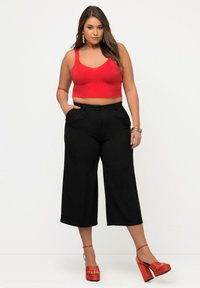 Rotes geripptes Crop-Top, schwarze weite Hosen und rote Plateauschuhe. Besitzt ein tailliertes Design, glatte Textur und sichtbare Nähte.