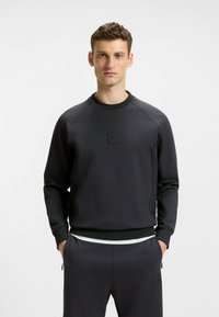 Herren schwarzer Pullover mit strukturierter Oberfläche, Rundhalsausschnitt, gerippten Bündchen und einem kleinen Logo-Patch auf der Vorderseite. Hat eine lockere Passform.