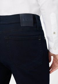 Jeans de color azul oscuro con un ajuste elegante, que cuentan con una etiqueta de cuero en la cinturilla, costuras mínimas y un solo bolsillo trasero.