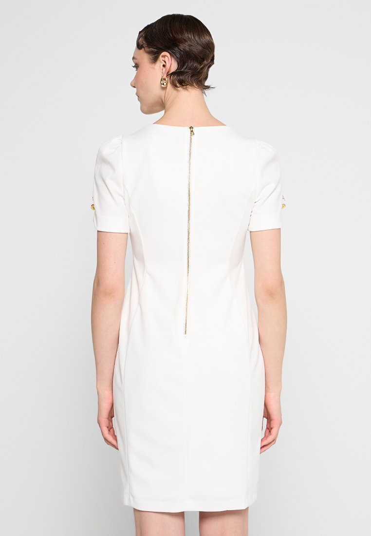 Biała dopasowana sukienka z krótkimi rękawami, z złotym zamkiem błyskawicznym z tyłu. Gładka tkanina i skrojony fason.