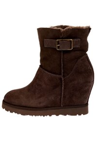 Brązowe zamszowe botki na wedges z podszewką z sztucznego futra, dekoracyjnym detalem w postaci klamry oraz teksturowaną gumową podeszwą, z zaokrąglonym noskiem i zakrzywioną formą.