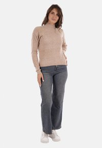 Maglione a coste beige con collo alto, maniche lunghe e una vestibilità aderente, abbinato a jeans flare in denim scuro e sneakers bianche.