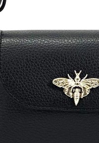 Sac en cuir noir avec une finition texturée et un accent en or en forme d'abeille sur le rabat. Design compact adapté aux petits essentiels.