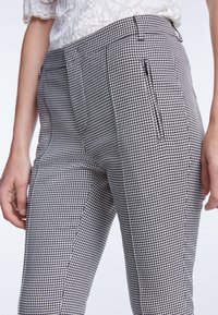 Zwart-wit houndstooth patroon broek met een getailleerde pasvorm, voorzien van zijzakken en een gladde textuur. Hoogtaille ontwerp zichtbaar.