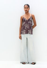 Purple floral-patterned camisole with thin straps paired with light blue wide-leg jeans. The top features embroidered accents on a textured fabric.