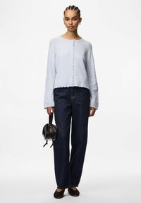 Light blue knitted cardigan with round neckline, scalloped hem, and button closure. Paired with dark wide-leg jeans and a small black handbag.