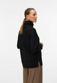 Czarny sweter z golfem o luźnym kroju, wykonany z miękkiego materiału. Posiada boczne rozcięcia i opuszczone ramiona, co zapewnia swobodę ruchów.