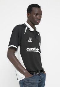 Ανδρικό πόλο μπλουζάκι σε ασπρόμαυρο με ριμπ υφή, με αντίθετο λευκό γιακά, λογότυπο και μεγάλο κείμενο στο μπροστινό μέρος. Συνδυάζεται με μπλε τζιν.