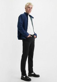 Chaqueta ligera azul marino con cremallera, camiseta blanca, jeans negros y zapatos de cuero negros. Corte recto con características de diseño mínimas.