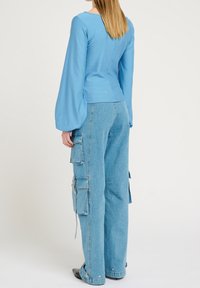 Haut bleu clair à manches longues avec une coupe ajustée, associé à un jean cargo ample doté de poches et d'une texture usée.