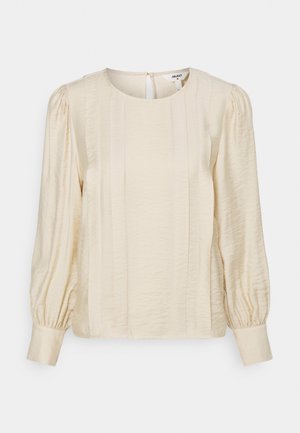 Blouse de couleur crème avec un col rond, des manches bouffantes et des plis verticaux. Tissu doux et texturé avec une fermeture à boutons au dos.