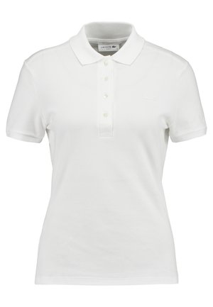 Polo bianco realizzato in cotone testurizzato, con colletto classico, chiusura a tre bottoni e un piccolo logo Lacoste sul petto.