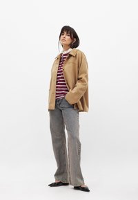 Beige-farbene Kunstlederjacke mit einem Kragen, kombiniert mit einem burgunderrot gestreiften Hemd, verwaschenen grauen Schlagjeans und schwarzen spitzen Ballettflats.