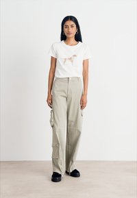 White t-shirt with a brown dog graphic, paired with high-waisted, loose-fitting light khaki cargo pants featuring side pockets.