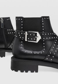 Bottines en cuir noir avec panneaux latéraux élastiques, clous argentés, une large sangle et détail de boucle, dotées d'une semelle en caoutchouc épaisse.