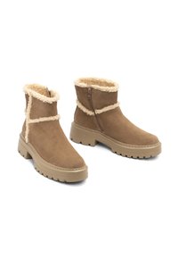 Botas de tobillo de ante marrón con forro de pelo sintético crema, cierre de cremallera y suela gruesa con relieve. Acentuadas con costuras de contraste.