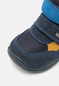 Zils un pelēks augsts apavu modelis ar velcro siksnām, izgatavots no zamša un sintētiskajiem materiāliem, ar oranžiem akcentiem un fakturētu zoli.