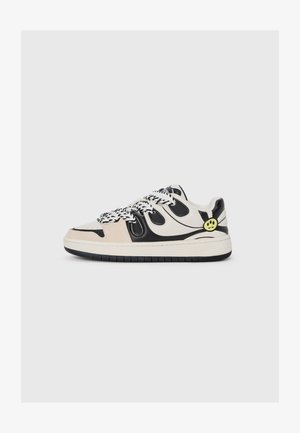 Baltas sneakeris ar melniem akcentiem, izgatavots no ziloņkaula un ādas materiāliem, ar unikālu viļņotu dizainu sānos, ar dzeltenu smaidošu seju uz papēža.