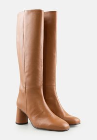 O pereche de cizme din piele bej, până la genunchi, cu vârfuri rotunde și tocuri bloc, pe un fundal alb simplu.