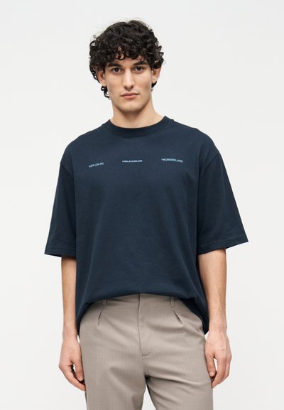 Μπλε βαμβακερό, φαρδύ T-shirt με κοντά μανίκια. Φέρει εκτυπωμένο κείμενο σε ανοιχτό μπλε: "NEW (25-26) HOLEWEILER *WONDERLAND".