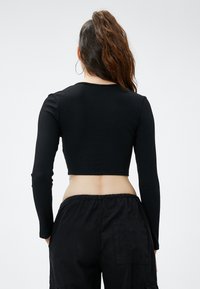 Zwarte geribbelde crop top met lange mouwen, ronde halslijn en een gestructureerde afwerking. Gepaard met losse zwarte broek met een elastische tailleband.