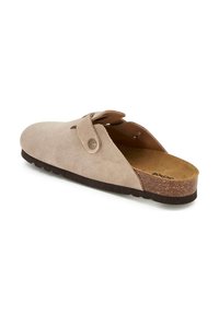 Sabots en suede beige avec un bout arrondi, une sangle réglable, une semelle intérieure en liège texturé, et une semelle extérieure en caoutchouc avec un motif nervuré.
