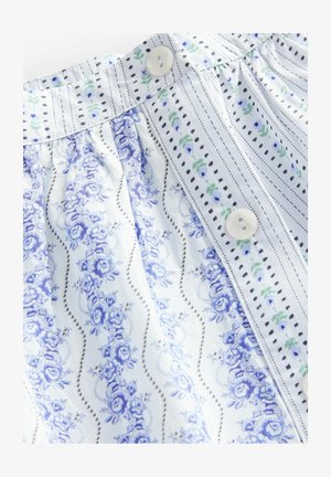 Blusa di cotone con motivo floreale blu, dettaglio a righe e chiusura con bottoni. Texture liscia con pieghe in vita.