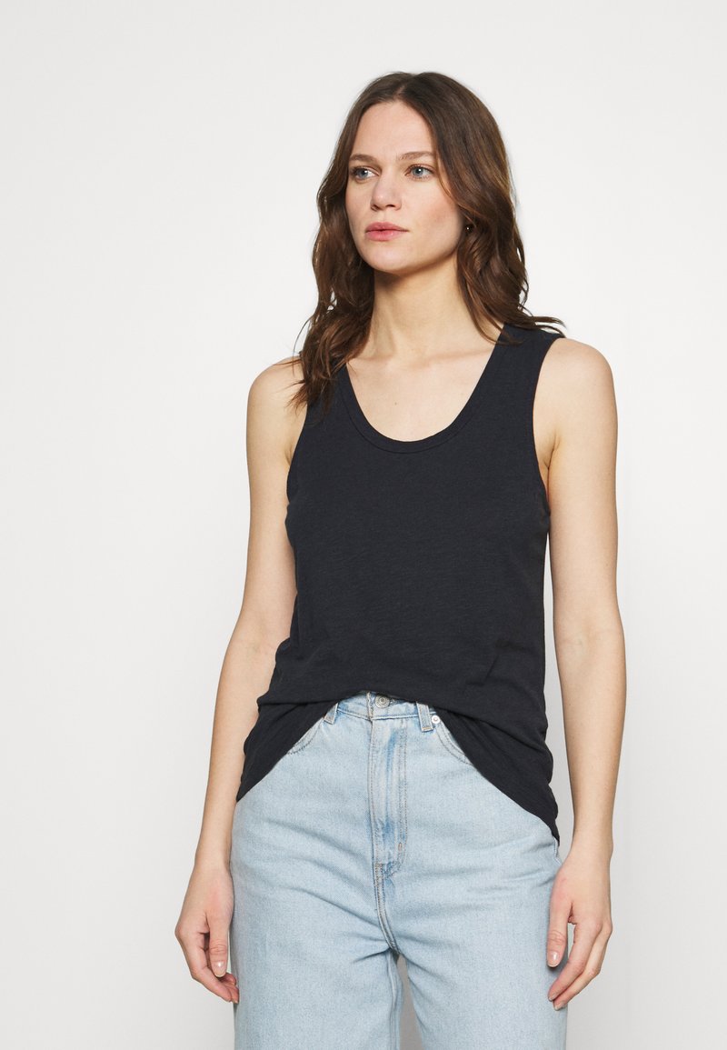 Canotta nera senza maniche in un tessuto morbido, con scollatura a barco e vestibilità rilassata, abbinata a jeans azzurri a vita alta.